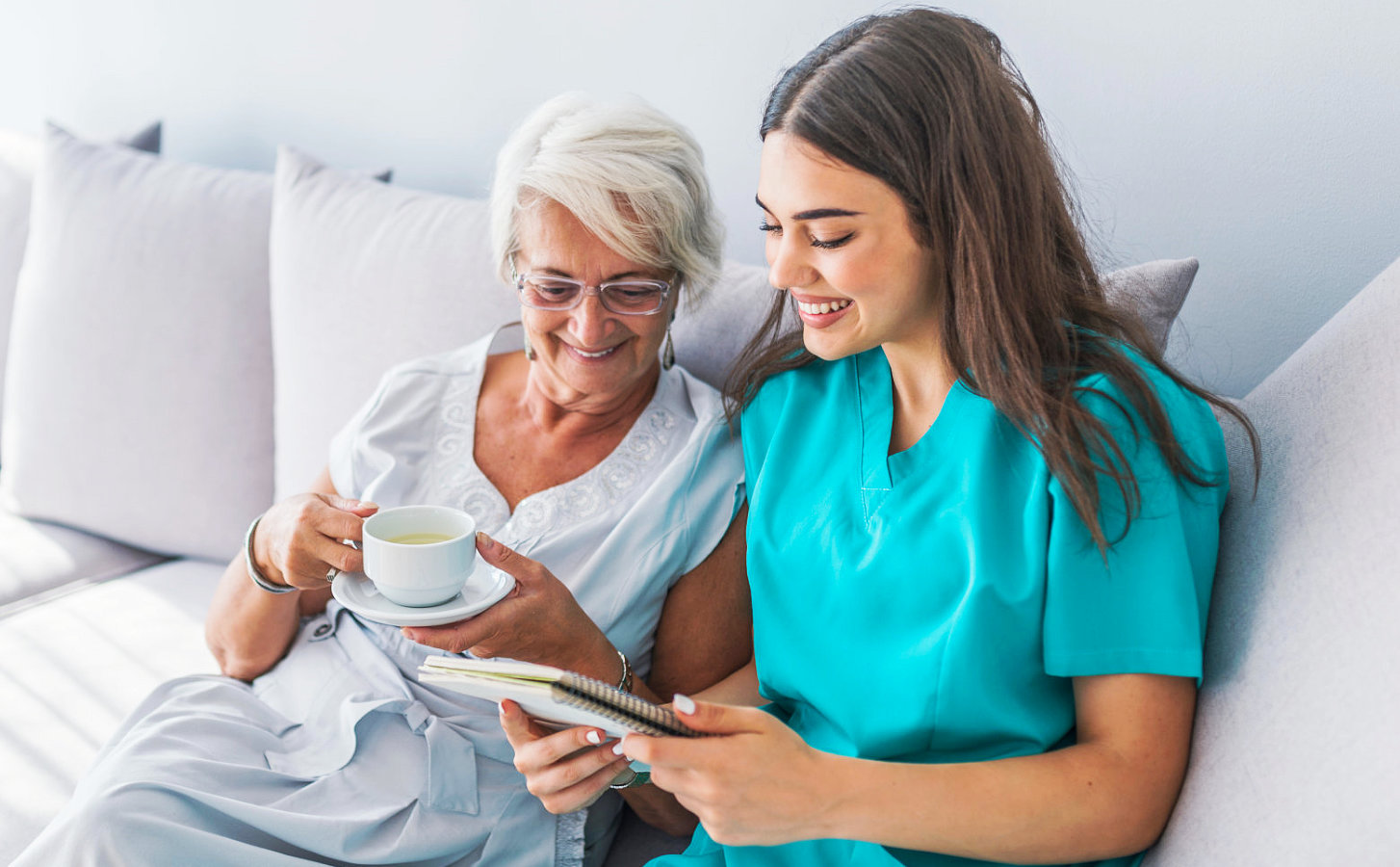 senior woman holding a cup of tea while the caregiver reading a note