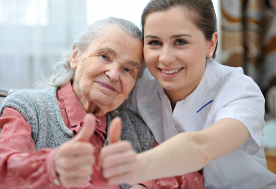 a caregiver and a senior woman showing thumbs up